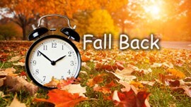 Fall Back. An alarm clock in a field of leaves.