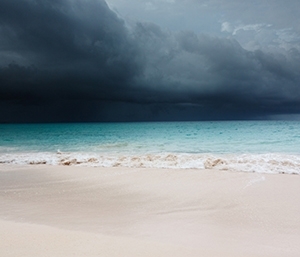 Dark storm cloud over the ocean and sand.