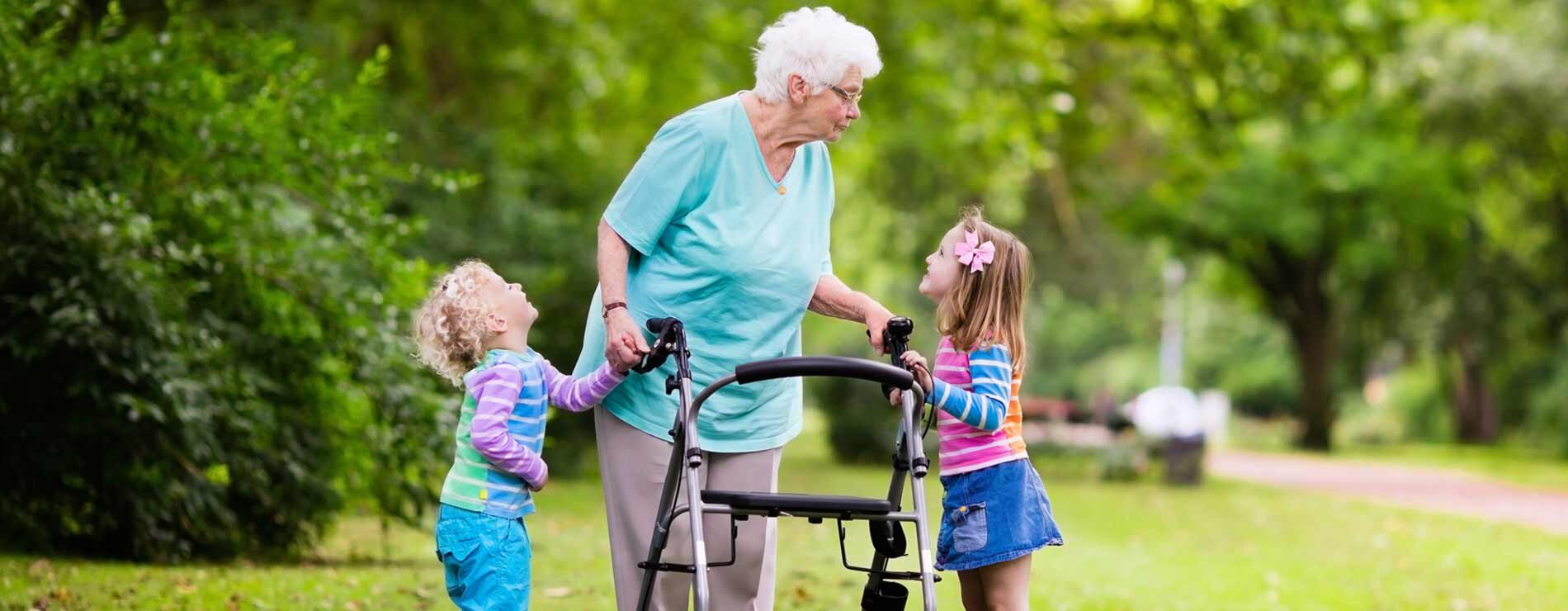 A woman using a walker and standing with two children outside.